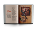 Open cookbook showing a recipe for roasted lamb with ingredients on a wooden board.